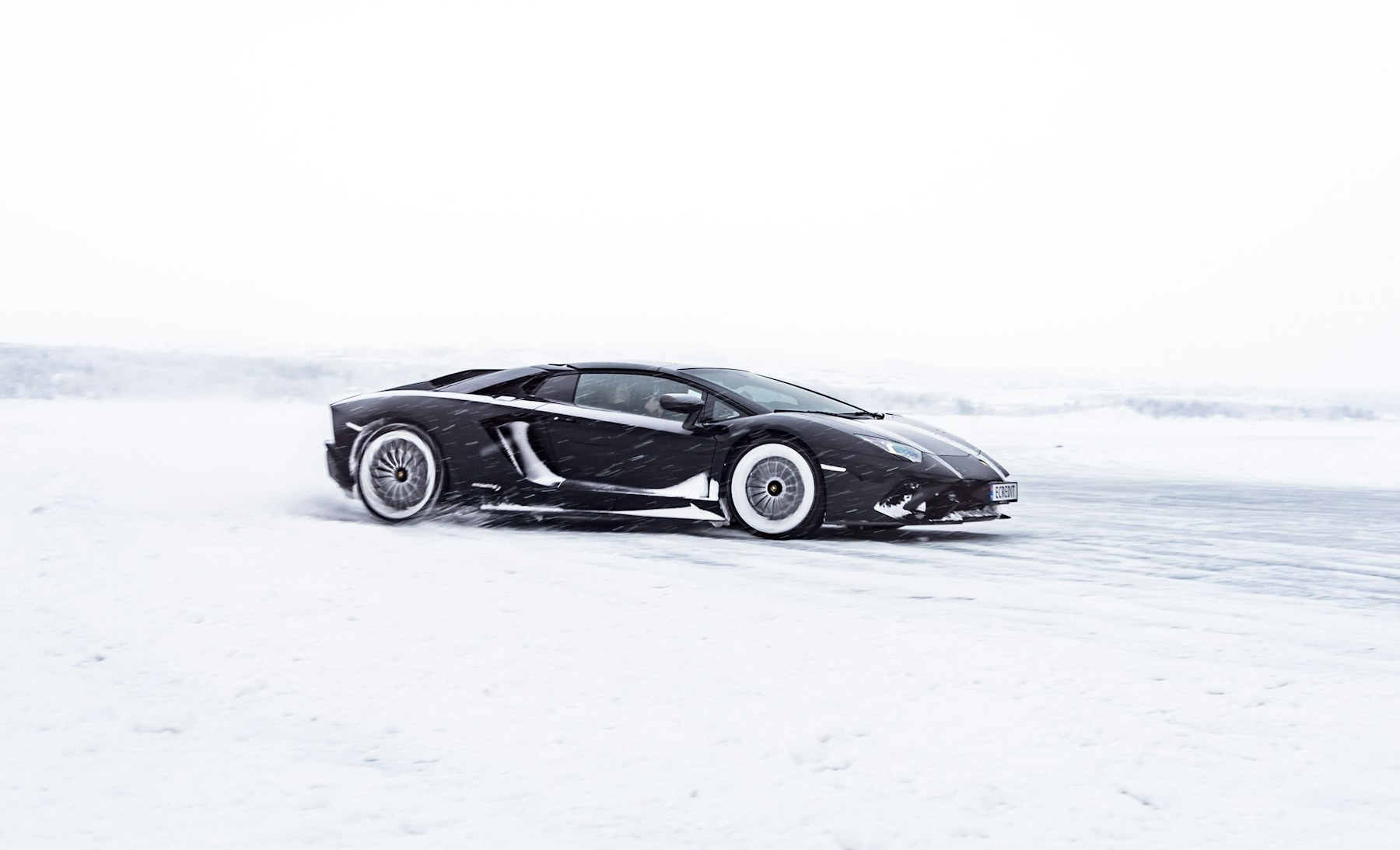Black performance car driving through a snowy landscape